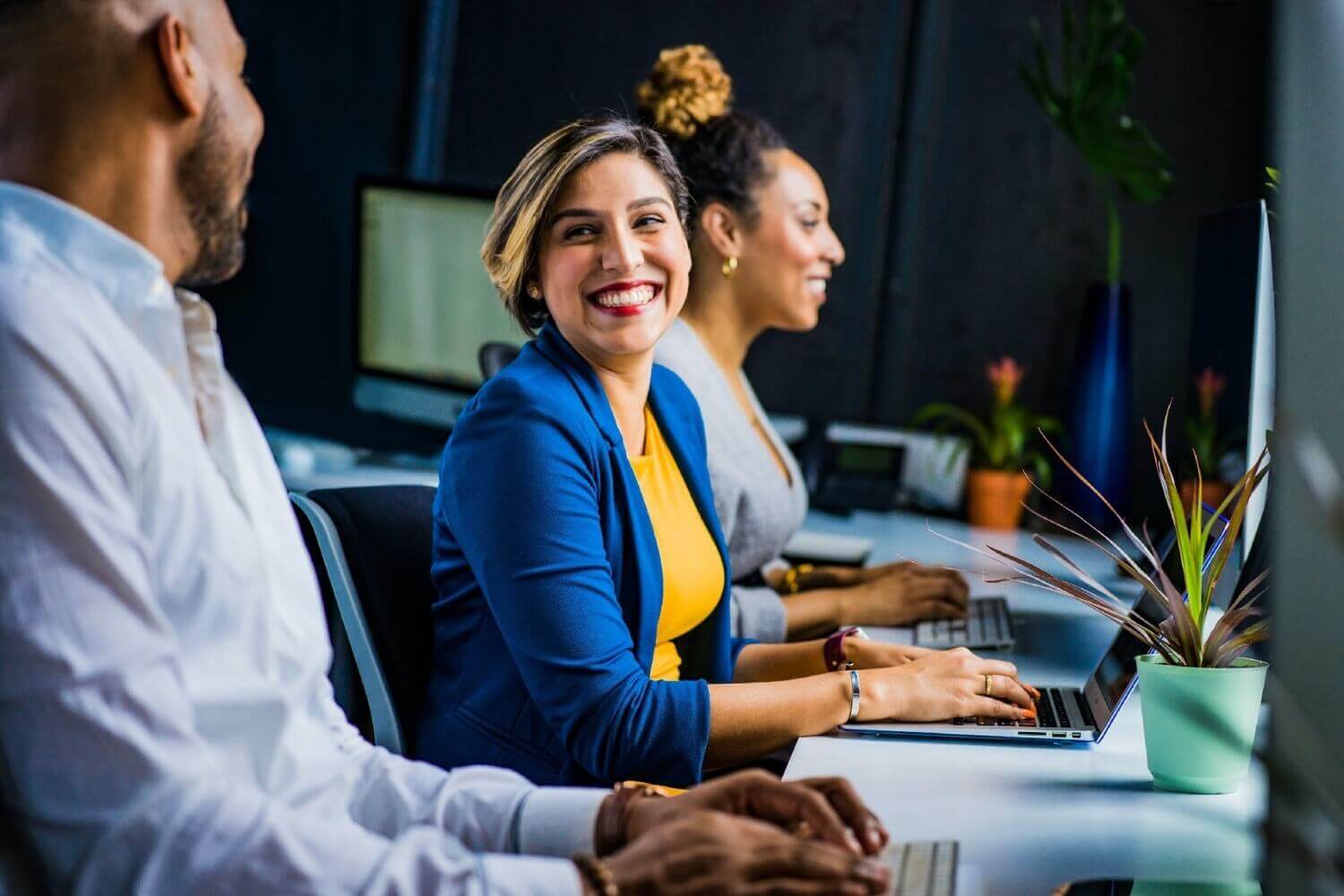 Customer Success Team Smiling And Chatting In Office In Front Of Laptops