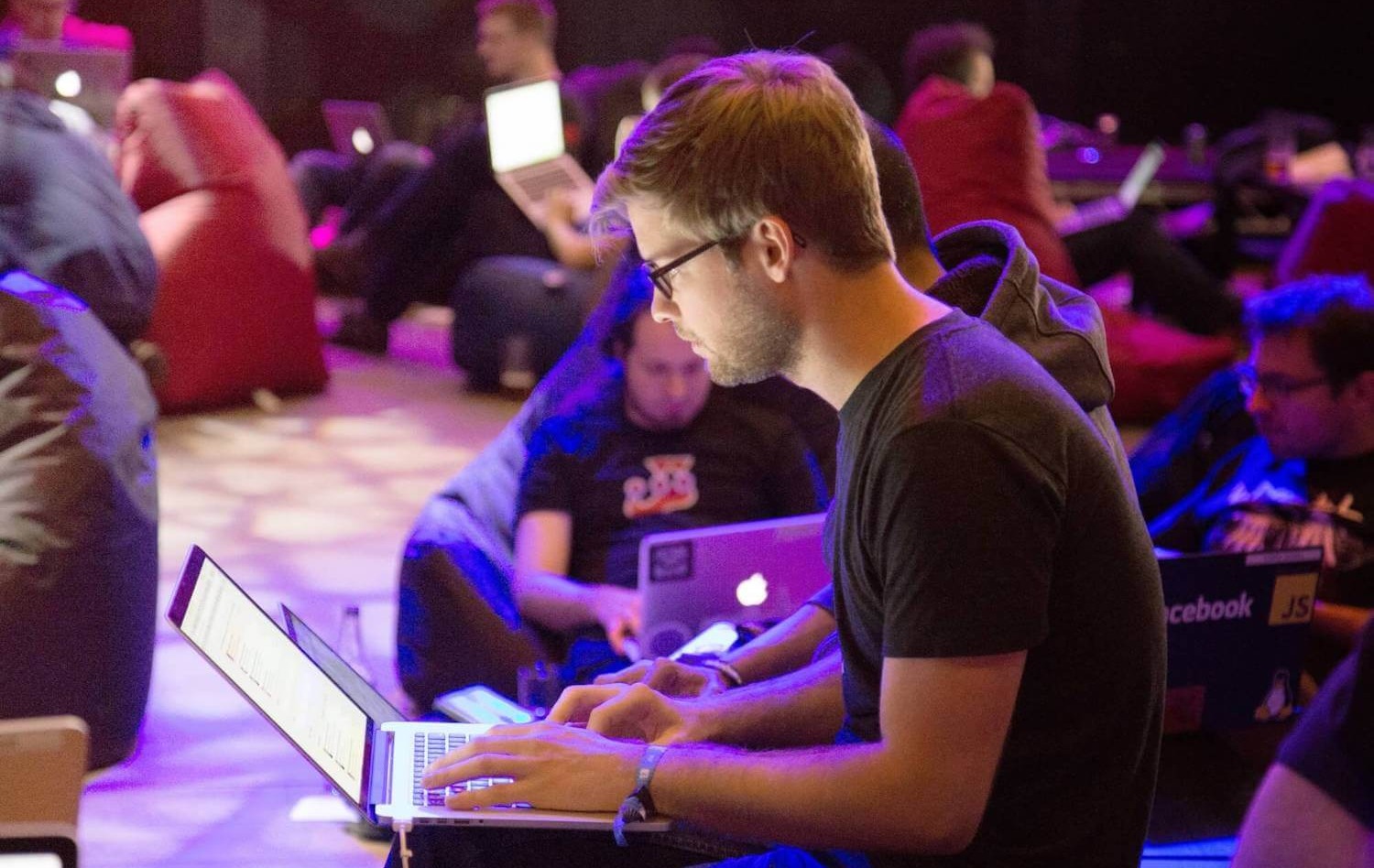 Developer at conference on laptop with other developers under blue light-1