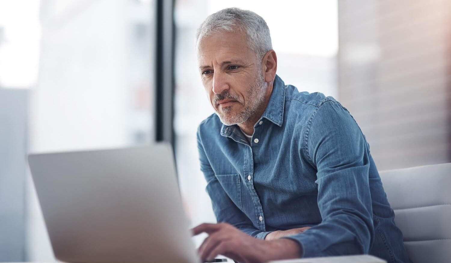 Grey haired man sitting smiling at laptop on desk