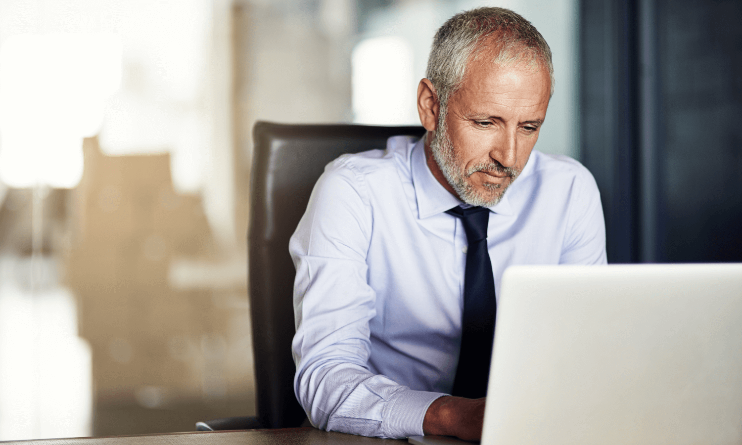 Male CEO typing at office desk using laptop to send secure email