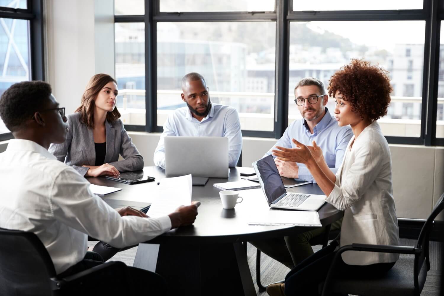 People in meeting around office table with laptops discussing potential savings from secure email