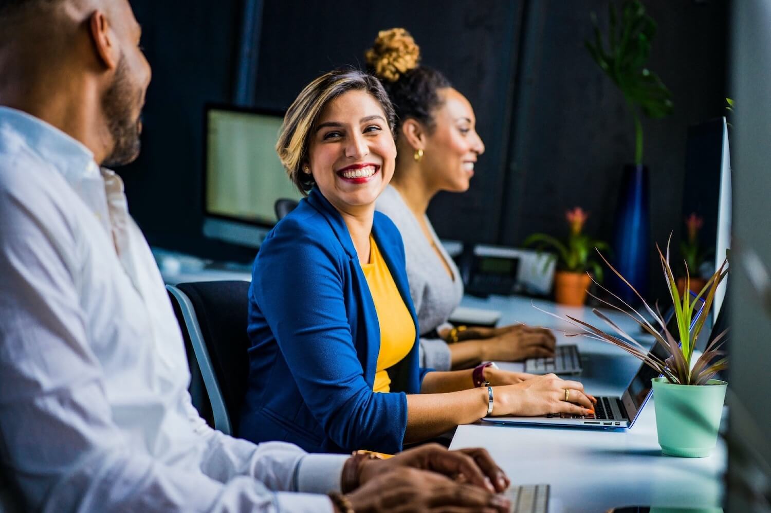 Female professional smiling and sitting in office with colleagues and using laptop to secure emails