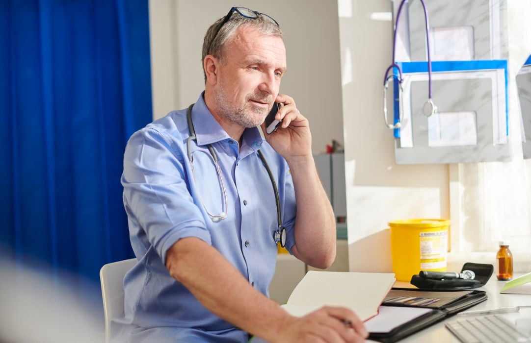 Senior doctor talking on phone next to computer