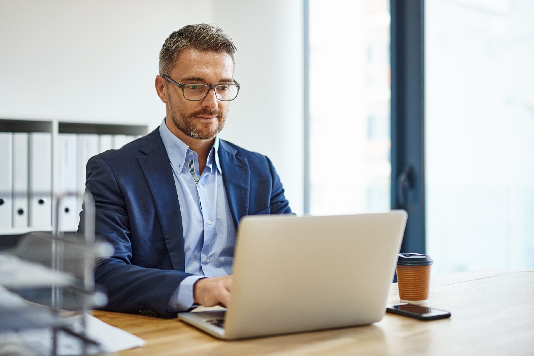 man in office with suit on working on laptop and smiling