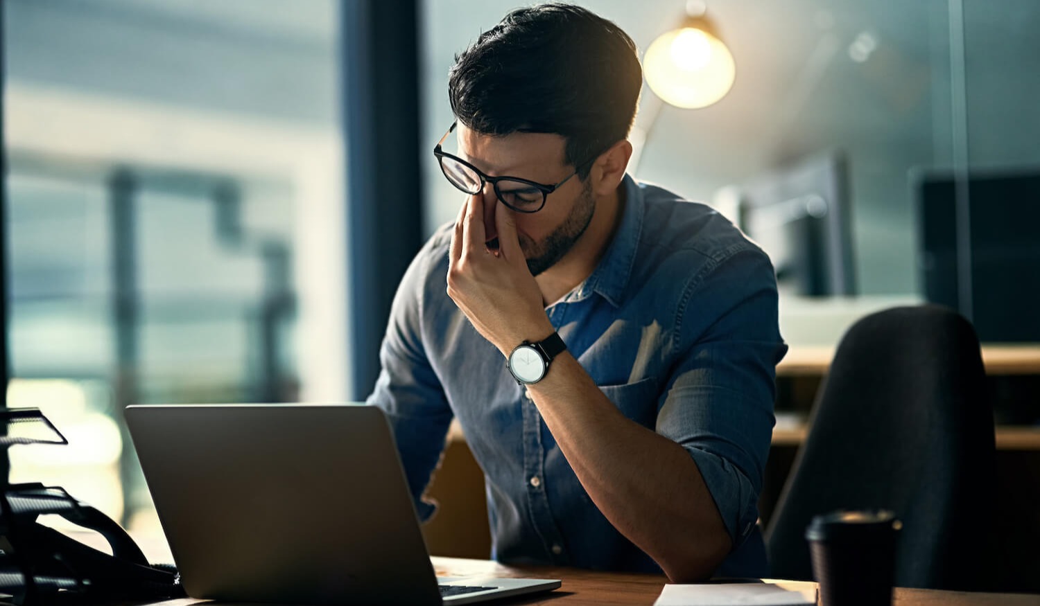 Man with head in hands stressed behind laptop