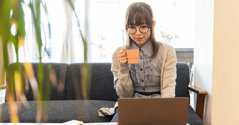 Woman sitting on sofa working from home using laptop